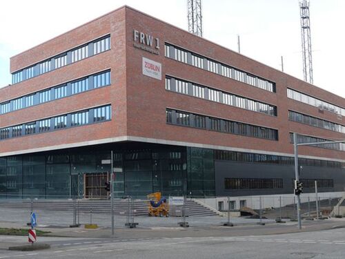 Ansicht der Gebäudeecke des roten Ziegelbaus mit Bauzäunen und Kränen