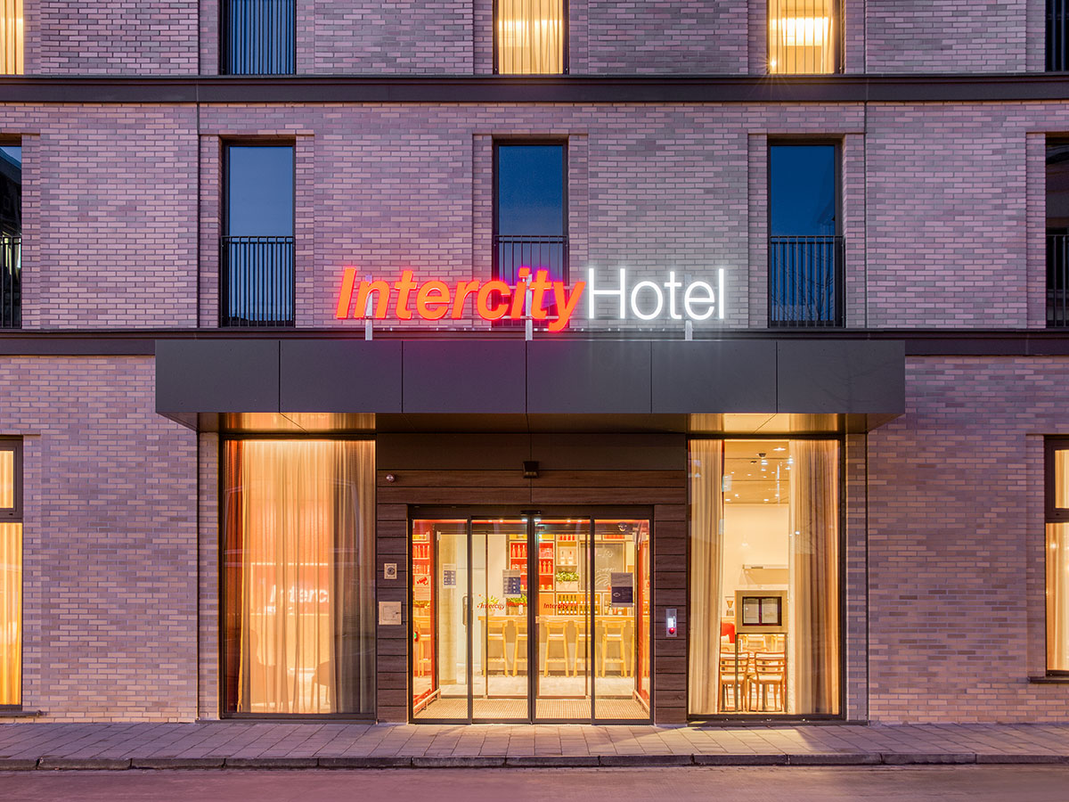 Abendaufnahme des Einganges von Außen, Ziegelfassade und beläuchtetes Foyer