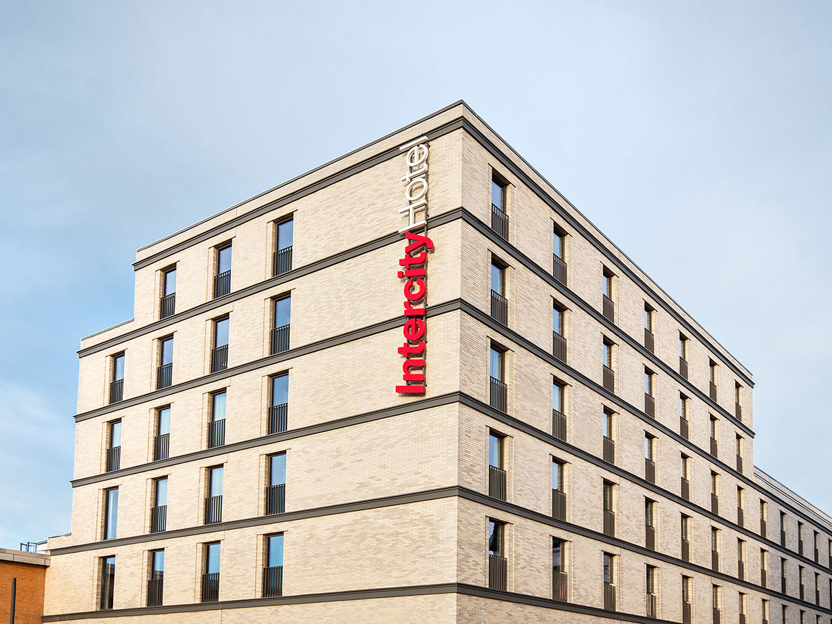 Blick auf die Gebäudeecke mit großem Logo "IntercityHotel", heller Klinker, dunkle Horizontallinien, Himmel