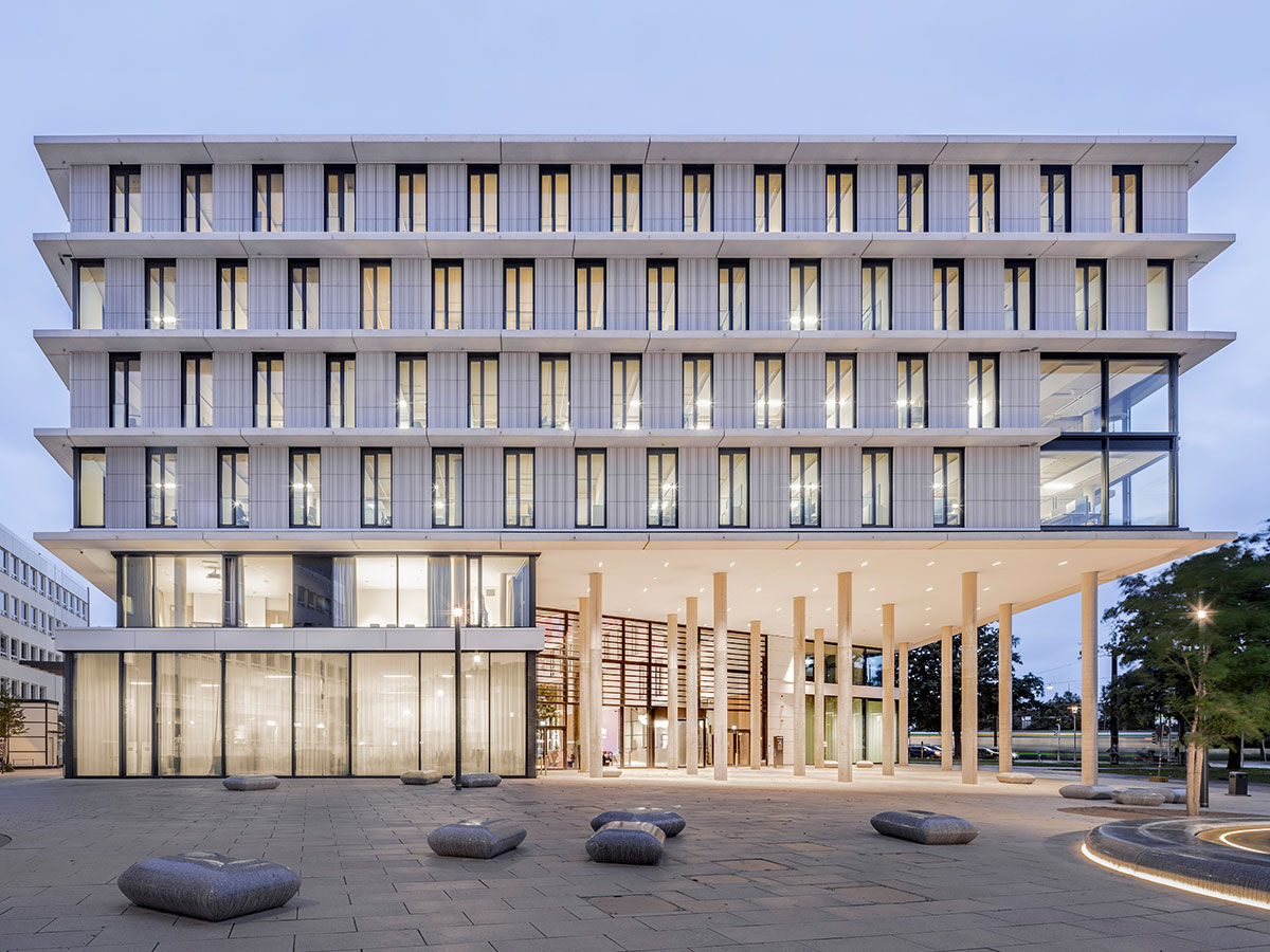 Abendansicht der weißen Gebäudefassade mit Sitzmöbeln und Lichtern außen vor Himmer zu blauer Stunde