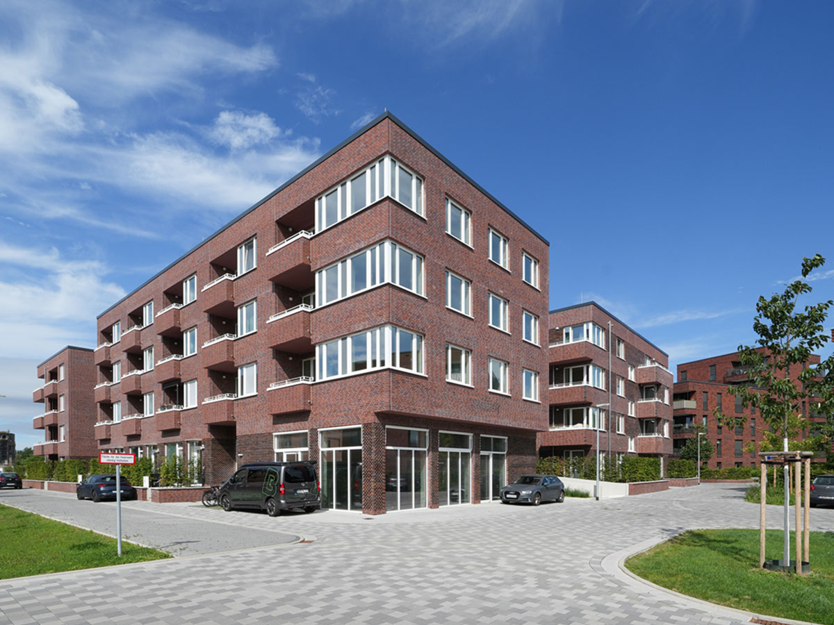 Foto von der Zufahrt aus auf die roten Ziegelgebäude mit Wegen, Bäumen, Rasen und Himmel