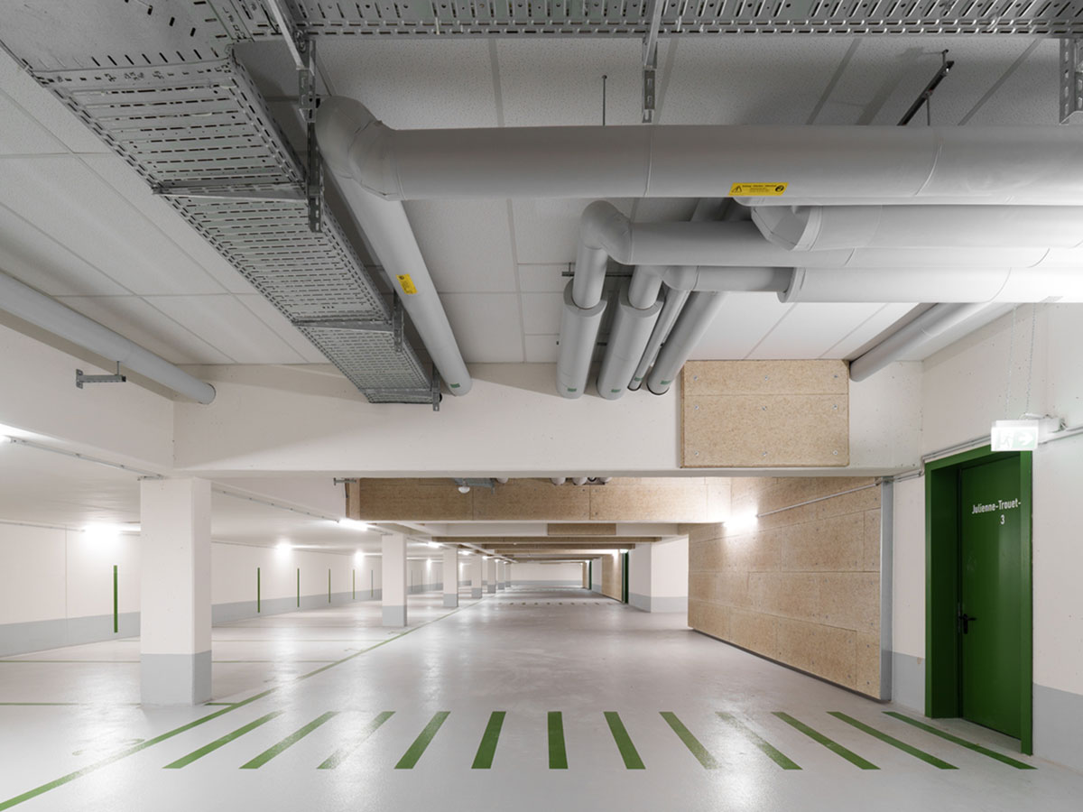 Blick in die moderne, helle und sauber Tiefgarage mit grünem Zebrastreiben und Lüftungsrohren unter der Decke